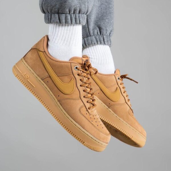 Tan Nike Air Force 1 sneakers with white crew socks and gray joggers, shown midair.