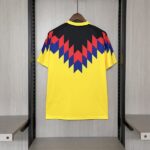 Yellow T-shirt with a black-red-blue zigzag chevron pattern across the upper back, hanging on a wooden hanger in a display closet.