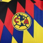 Close-up of a Club America crest on a colorful geometric jersey (yellow circle, map of the Americas, CA letters).