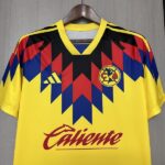 Yellow soccer jersey with a bold red, blue, and black zigzag pattern across the chest, Adidas logo on the left, team crest on the right, and 'Caliente' sponsor text across the front.