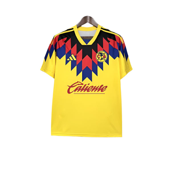 Yellow football jersey with a red, blue, and black zigzag pattern across the chest, featuring the club crest, Adidas logo, and 'Caliente' sponsor.
