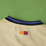 Back view of a beige mesh sports jersey with a black-and-purple striped collar and a small yellow-red-blue flag patch on the chest area.