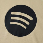Spotify logo: black circle with three curved white lines on a beige background.