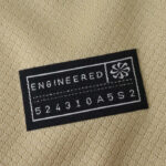 Black clothing label with the word 'ENGINEERED' and a small emblem on the right, plus the serial '524310A5S2' stitched on beige fabric.