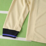 Beige long-sleeve shirt sleeve with a black cuff and purple stripe, laid on a green surface.
