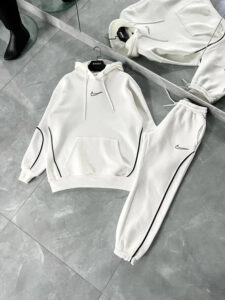 White Nike tracksuit hoodie and matching jogger pants, with black piping, laid on a showroom floor.