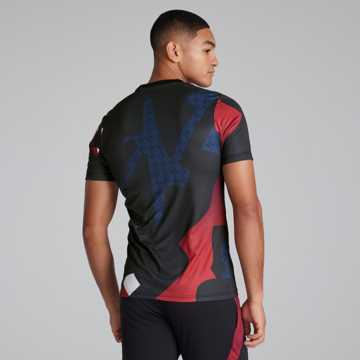 Back view of a man wearing a black, red, and dark blue abstract-pattern athletic jersey against a gray background.