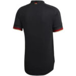 Back view of a black short-sleeve soccer jersey with red and gold trim on the sleeves and collar, and a small flag detail at the back neckline.
