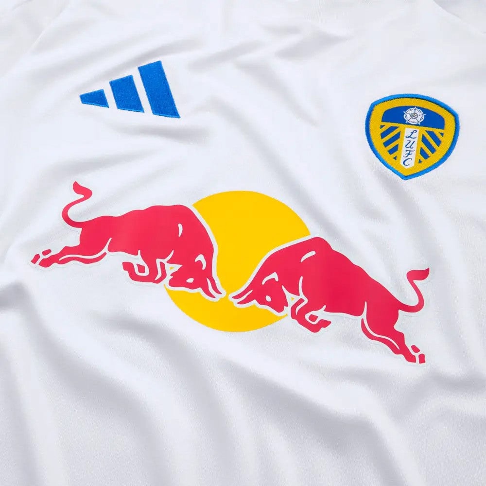bwDNEWSpWulQVXU | UAE SPORT STORE White sports jersey featuring the Red Bull logo in pink/red across a yellow sun motif, with Adidas branding above and a Leeds United crest on the chest.