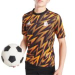 Athlete in a black, red, and yellow zigzag-pattern jersey holding a soccer ball against a white background.