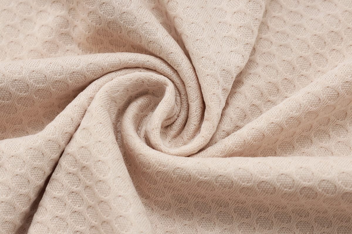 Beige textured fabric with a circular dot pattern, folded in soft spirals.