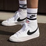 c0292029-bb01-4303-9b31-a9efc0160cea | UAE SPORT STORE White Nike high-top sneakers with black swoosh and white laces, worn with branded white socks on pavement.