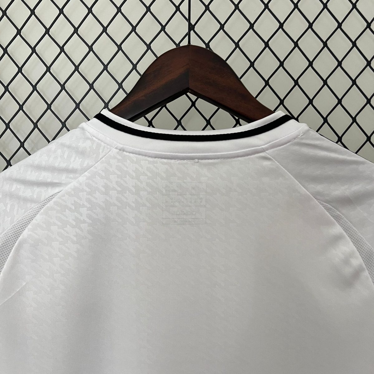 Close-up of a white shirt on a wooden hanger against a chain-link fence backdrop