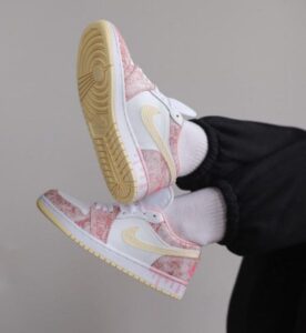 White sneakers with pink marbled pattern and yellow Swoosh, worn with white socks and black joggers (Nike).