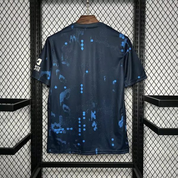 Back view of a dark blue athletic jersey with light blue splatter pattern hanging on a wooden hanger in a metal display rack.