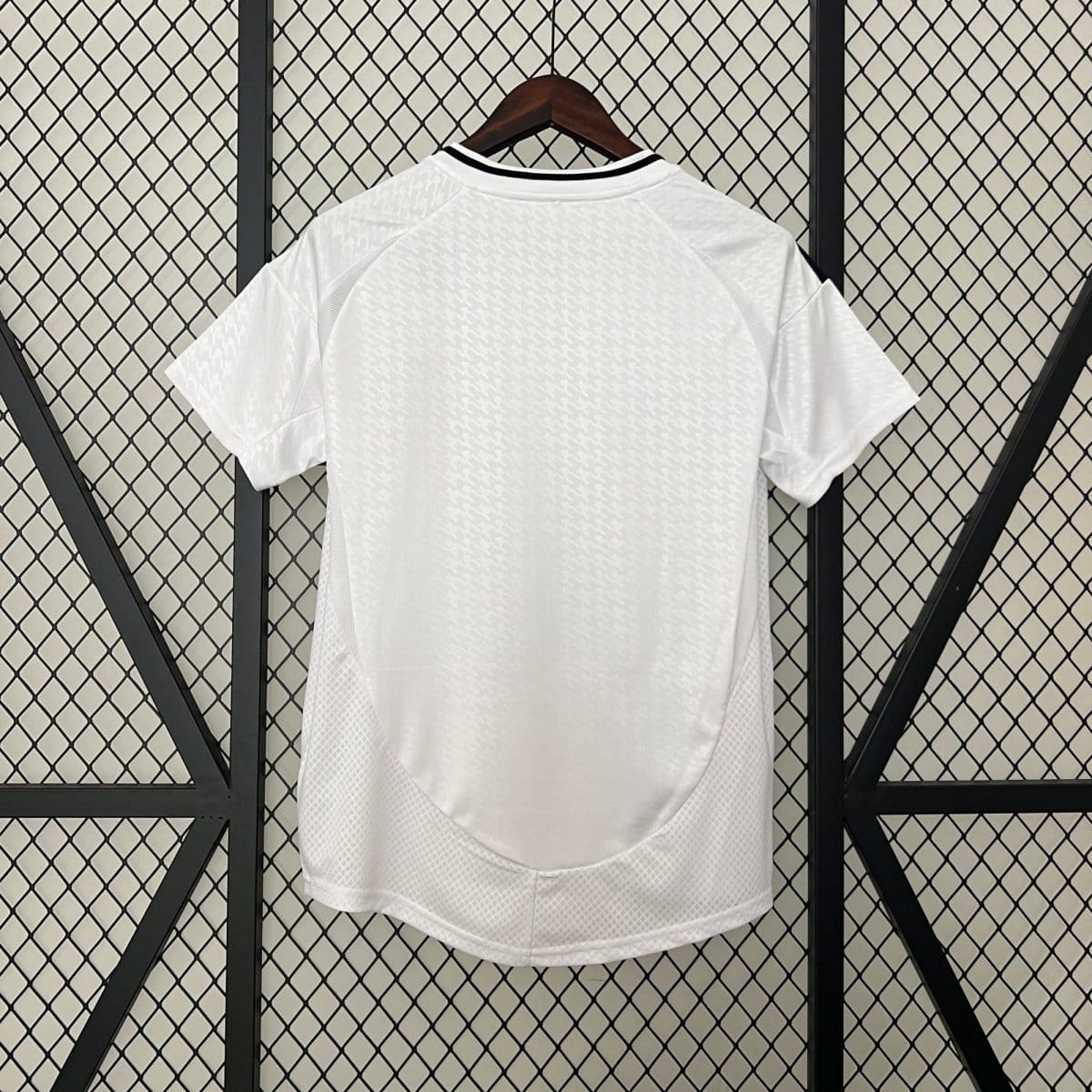 White short-sleeve shirt on a wooden hanger, displayed against a diamond-pattern metal grid backdrop, with subtle textured pattern on fabric.