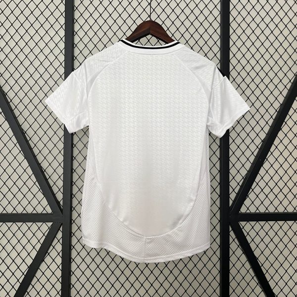 White short-sleeve shirt on a wooden hanger, displayed against a diamond-pattern metal grid backdrop, with subtle textured pattern on fabric.