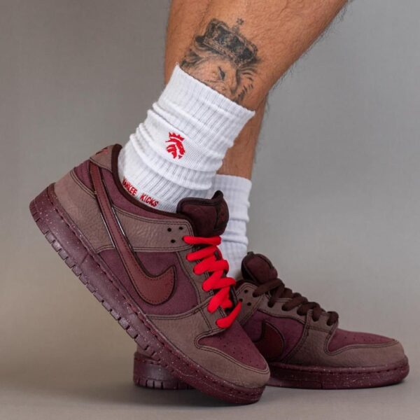Maroon Nike sneakers with red laces worn with white ribbed socks, leg tattoo visible above the ankle in a raised pose