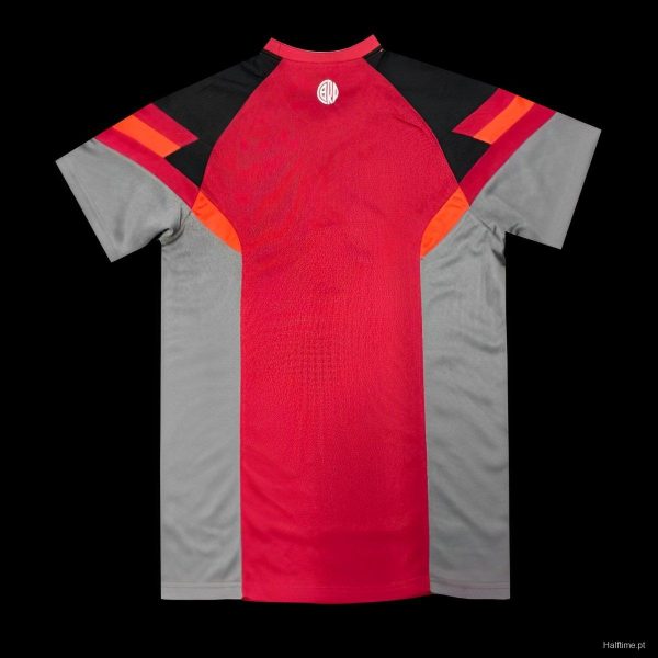 Front view of a red and gray athletic jersey with black shoulders and orange accents; small white circular logo at the neckline.