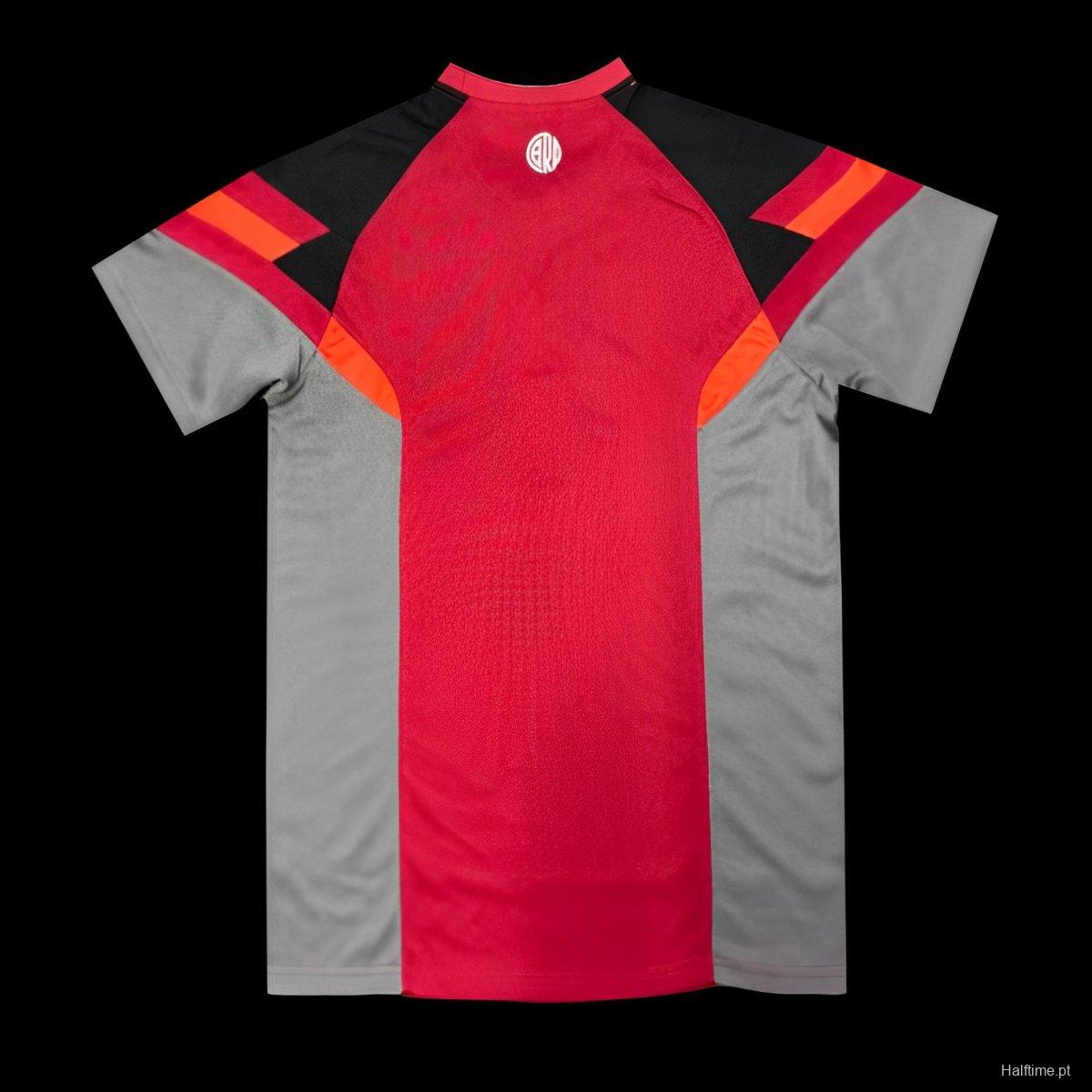 c1572812fa1b6a7b13c617b9 | UAE SPORT STORE Front view of a red and gray athletic jersey with black shoulders and orange accents; small white circular logo at the neckline.