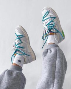 Person wearing white sneakers with teal laces and gray sweatpants, feet raised in the air