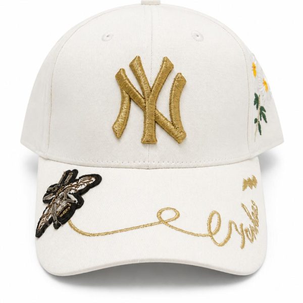 White baseball cap featuring a gold NY Yankees logo on the front, with floral embroidery on the side and gold cursive writing on the brim.