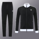 Black Adidas track jacket with white stripes along the sleeves, white collar and cuffs, shown with matching black track pants.