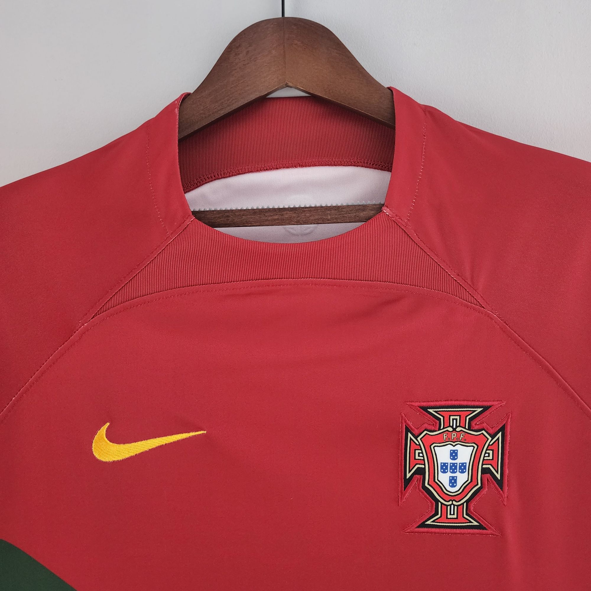 c2760be1_15a38ffa-75e7-45d1-b718-cbba57e1175f | UAE SPORT STORE Red athletic jersey on a wooden hanger featuring a yellow Nike swoosh and the Portugal crest on the chest area.