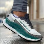 Close-up of a white New Balance running shoe with teal sole on a wet sidewalk, worn by a person in rolled jeans.