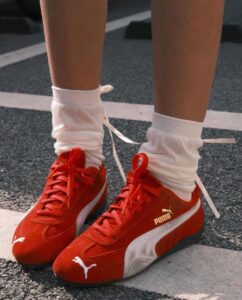 c2ba5535-bc3d-43fc-a5ef-2b625b8db93f | UAE SPORT STORE Person wearing red Puma sneakers with white socks on a track surface, close-up of feet and lower legs.