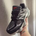 Black and gray chunky sneaker held in a hand, showing the New Balance 'N' logo and rugged sole.