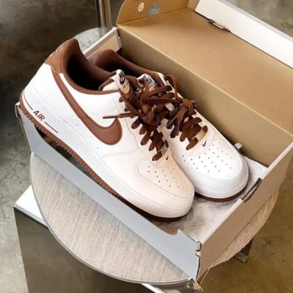 White Nike Air sneakers with brown swoosh and laces in an open shoebox on a table.