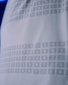 Close-up of pale blue fabric printed with a repeating grid of small squares containing numbers and symbols.