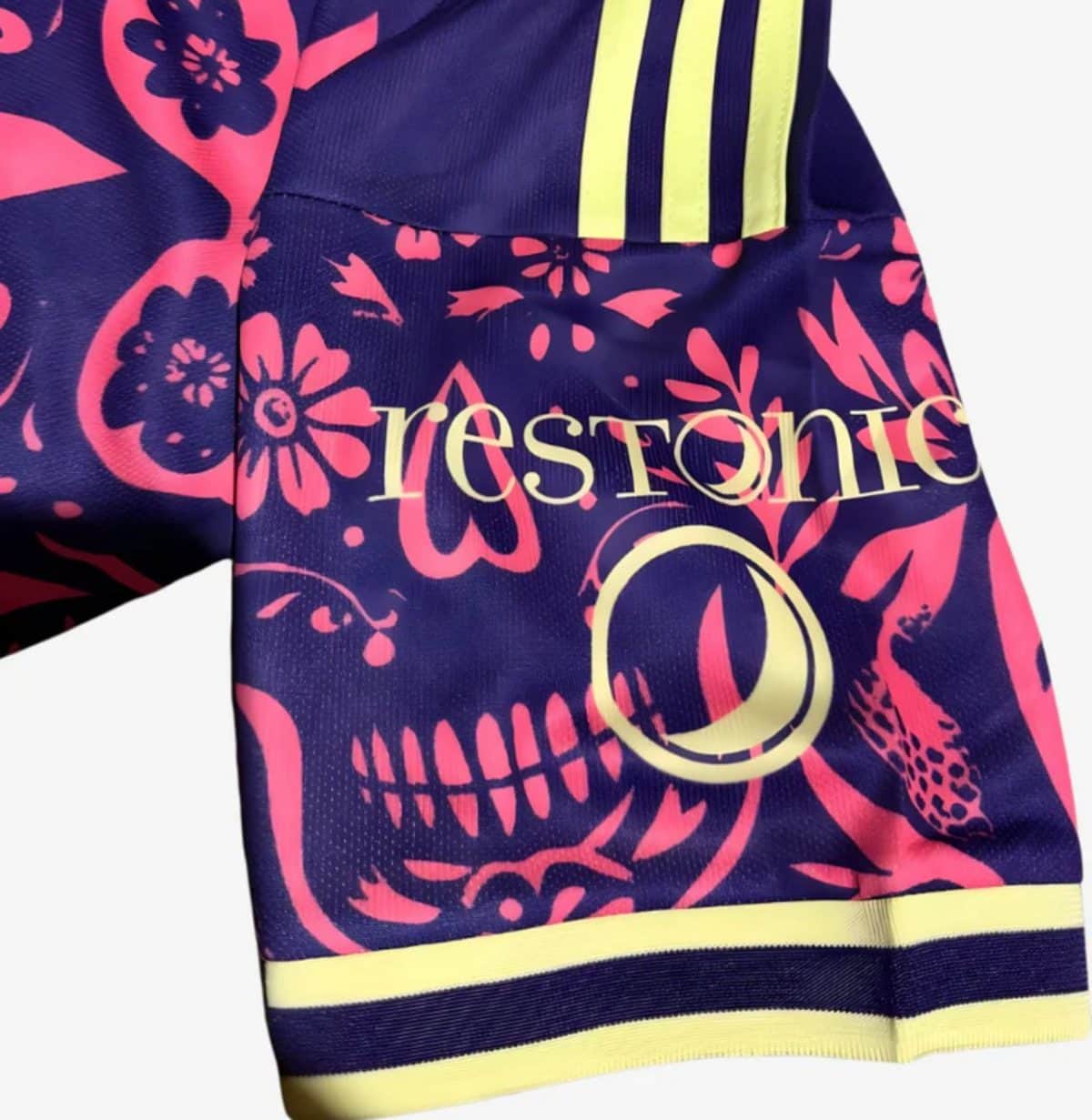 Close-up of a dark purple jacket featuring a bright pink floral skull design and neon yellow trim along the hem and shoulder stripes.
