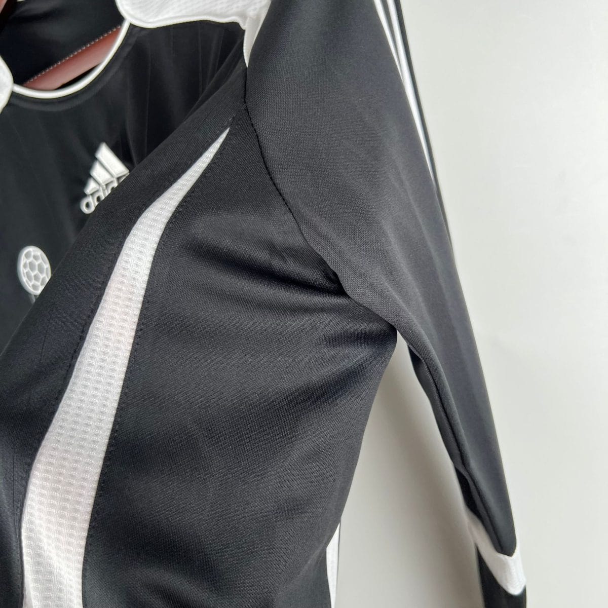 Close-up of a black Adidas jacket with white piping and the Adidas logo visible on the chest area.