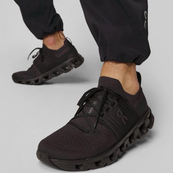Black athletic sneakers with a bold, hollowed pod-like sole, worn by a person in black joggers stepping forward.