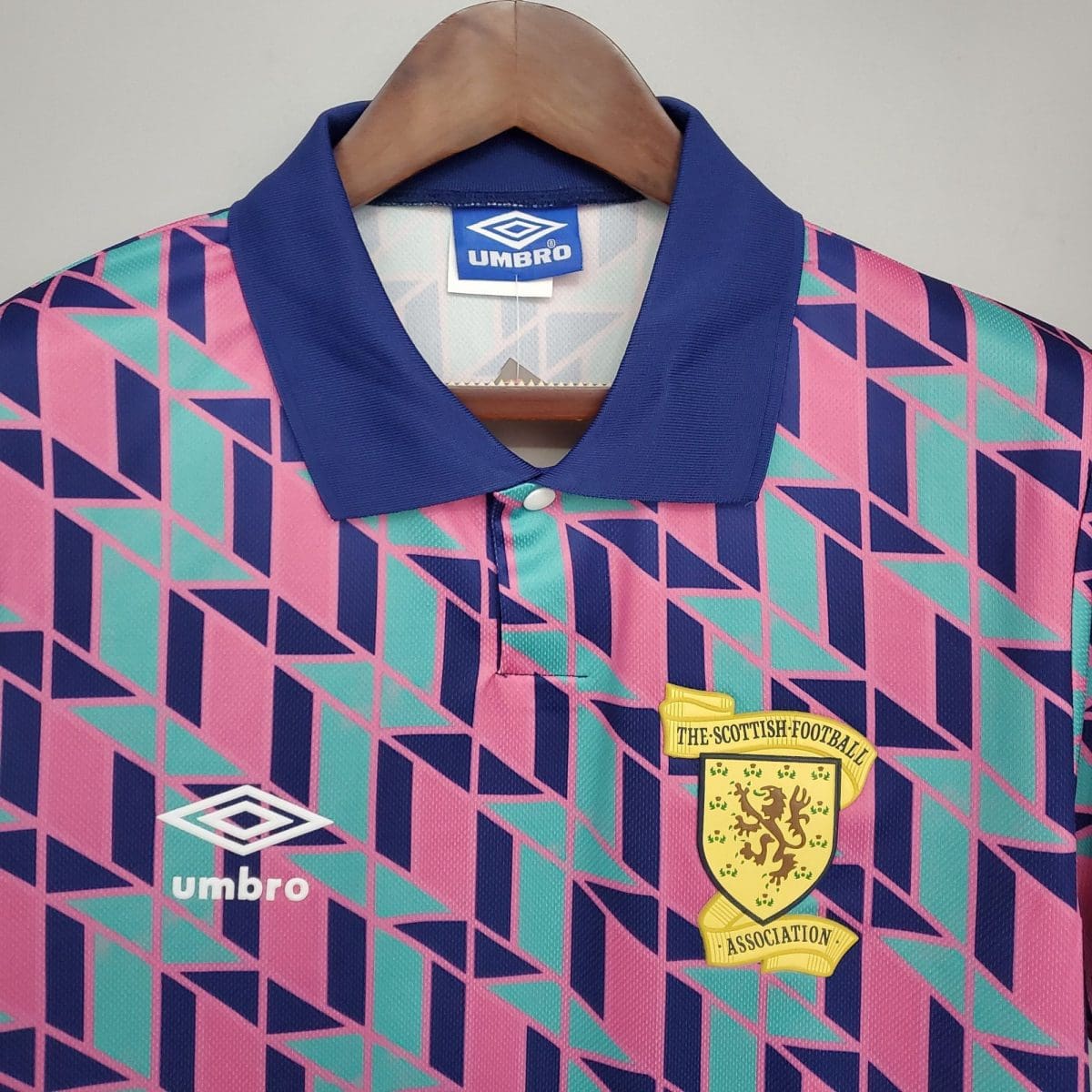 Colorful geometric-patterned polo shirt on a hanger with a blue collar, displaying an Umbro tag and a Scottish football badge on the chest