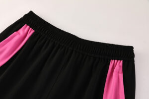 Black athletic shorts featuring pink side panels and a gathered elastic waistband.