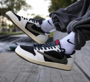 Pair of black-and-white Nike sneakers with white socks, resting on a wooden boardwalk outdoors, viewed from the side.