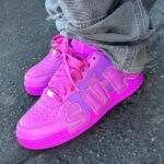 Bright pink athletic sneakers with chunky laces on gray denim jeans, standing on asphalt surface.