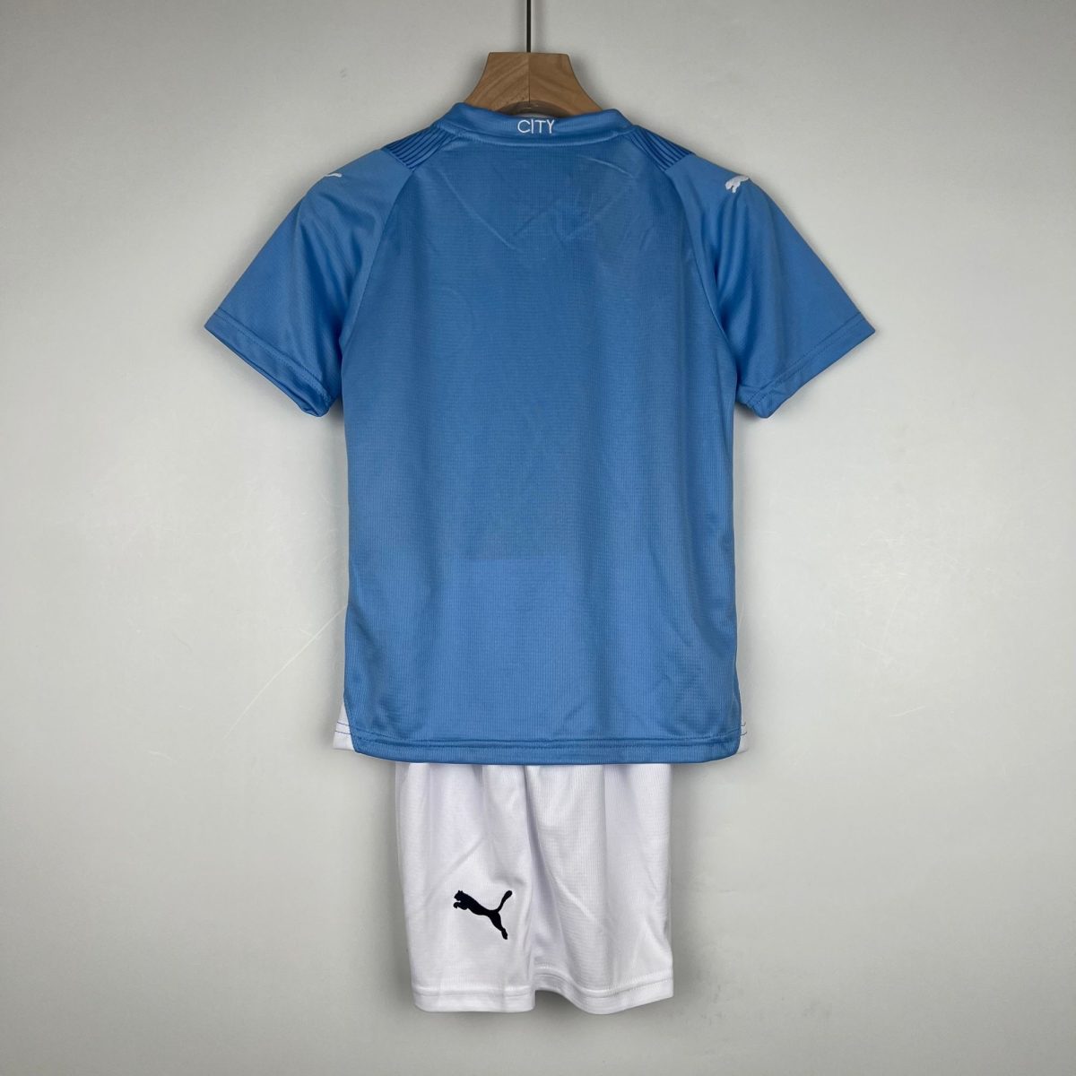 Blue sports jersey hanging on a wooden hanger with white shorts beneath; back collar reads CITY on the neck area.