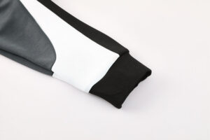 Close-up of a gray, white, and black color-blocked sleeve with a black ribbed cuff, likely from a sports jacket.