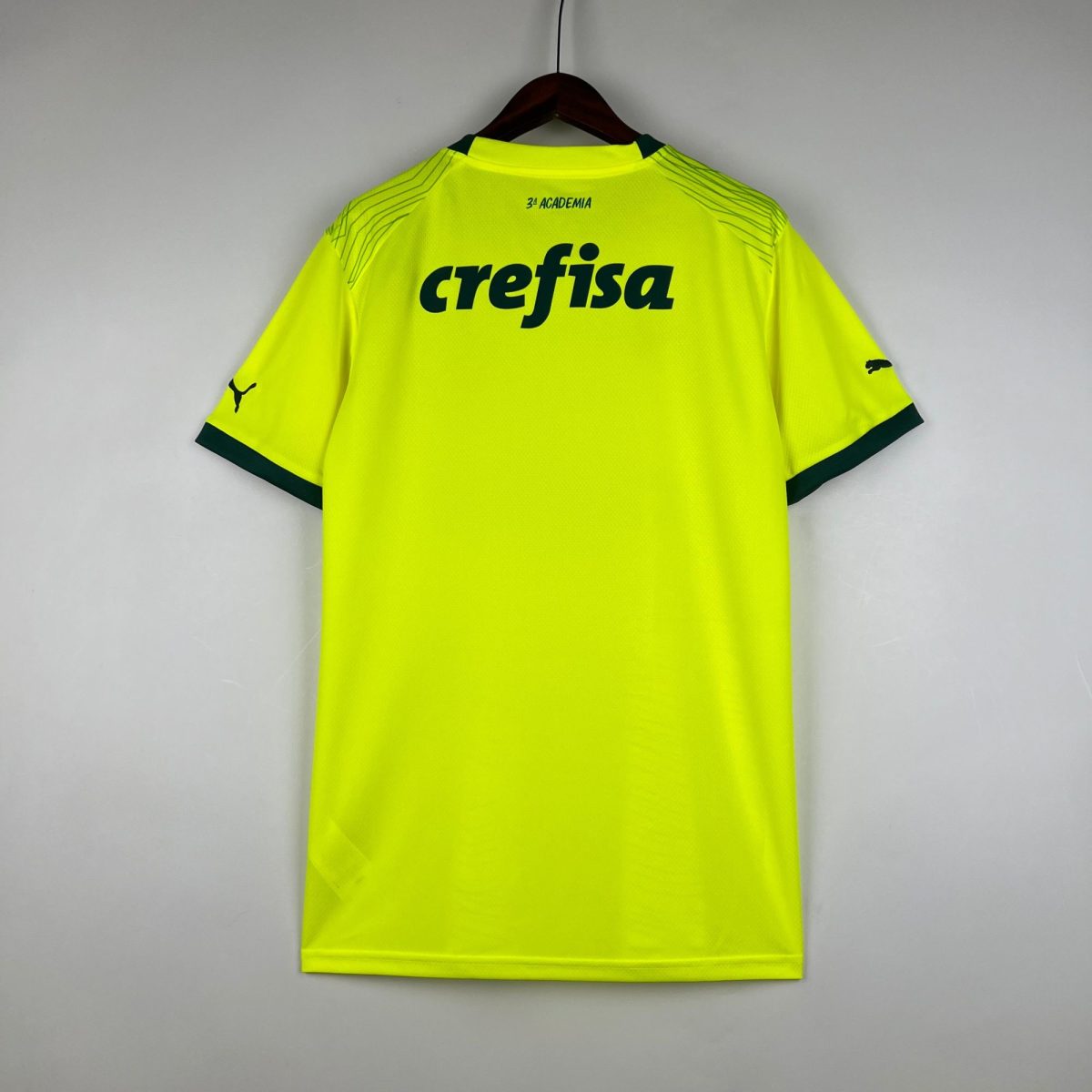 Bright neon yellow sports jersey hanging on a wooden hanger against a gray wall, showing 'crefisa' logo on the back.