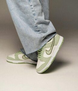 Person wearing light-wash jeans and green-and-white sneakers stepping forward on a beige surface.