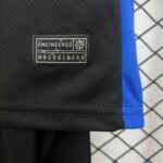 Close-up of black fabric with a stitched label reading 'ENGINEERED' and a small emblem, blue strap on the right, with a chain-link fence in the background.