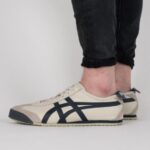 Beige athletic sneakers with navy stripes worn by a person in rolled-up black jeans, side view.