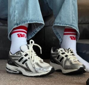Person wearing light-wash jeans and white socks with red stripes and logo, standing in silver and white running shoes on a carpeted floor.