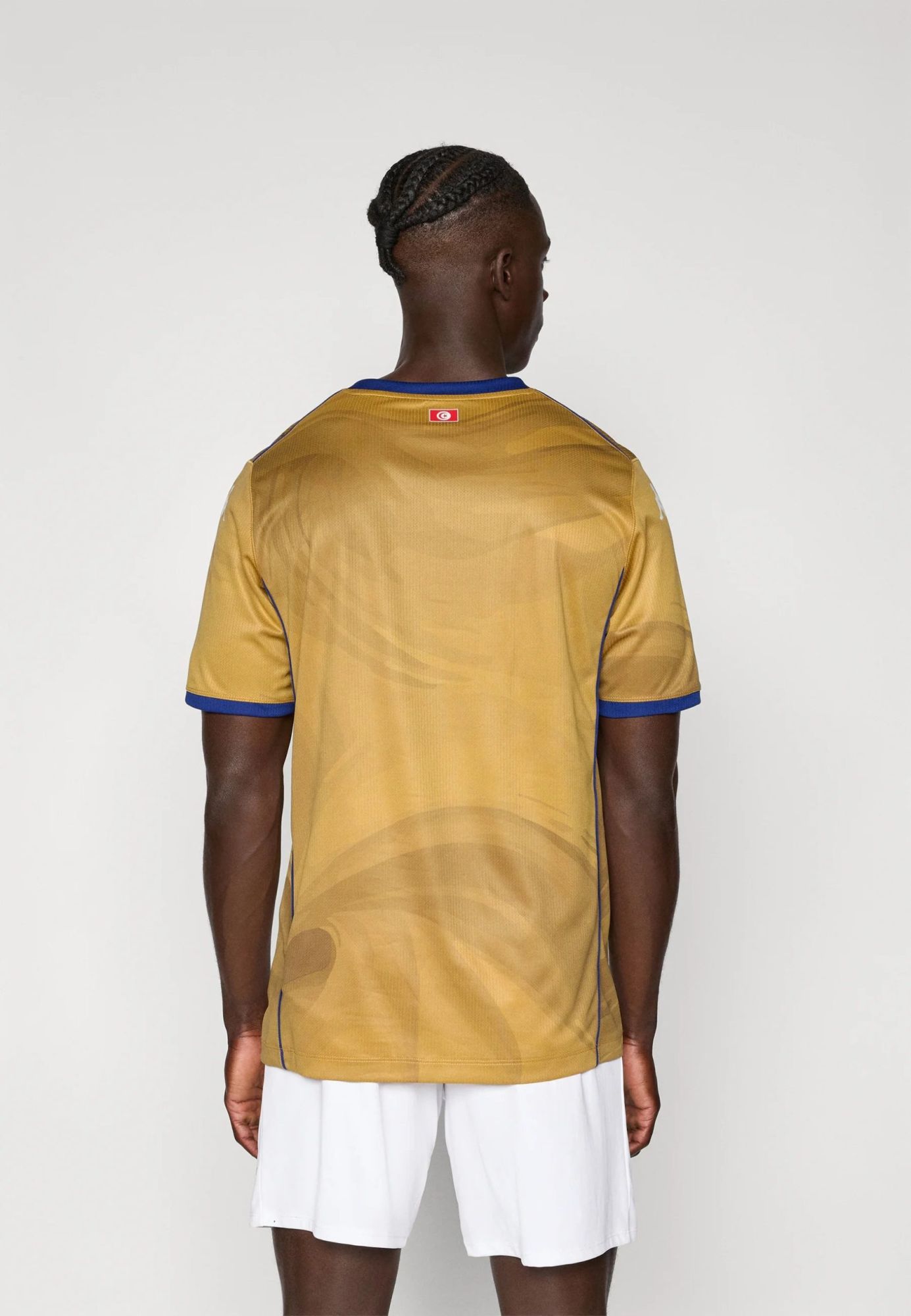 c74ccb5041e54a53b1369e0a02f56381 | UAE SPORT STORE Back view of a person wearing a gold athletic jersey with blue trim and a small flag patch on the upper back, with white shorts below.