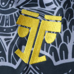 c75329cc | UAE SPORT STORE Close-up of a yellow embroidered symbol on dark patterned fabric.