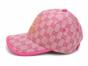 Pink baseball cap featuring Gucci's repeating GG pattern in pink, with a yellow Gucci logo on the front and a pink brim.